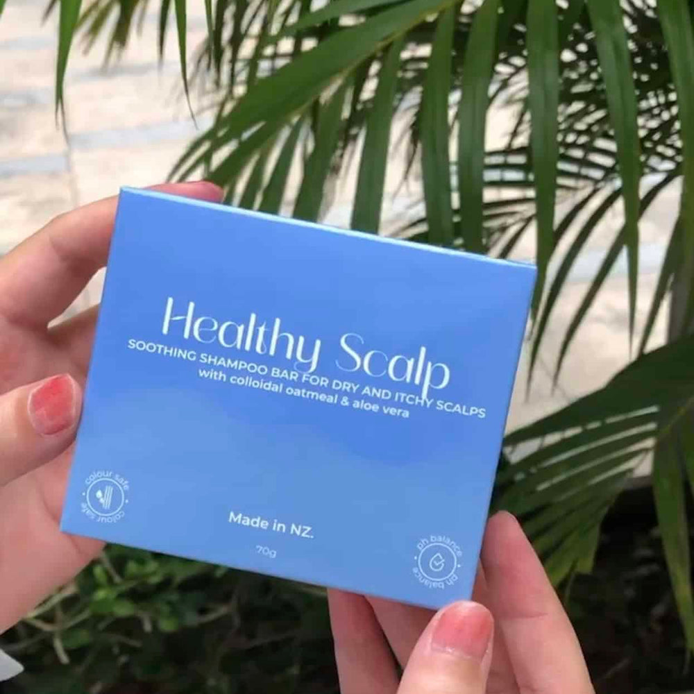 Hand holding a blue box labeled 'Healthy Scalp' with green foliage in the background